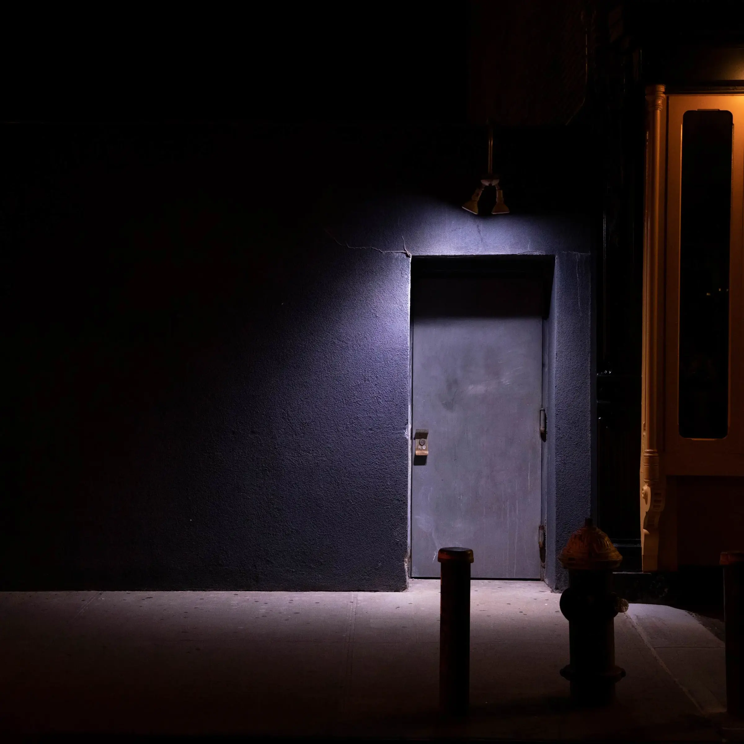 A dimly lit unmarked door in a dark alley, like a hidden speakeasy entrance