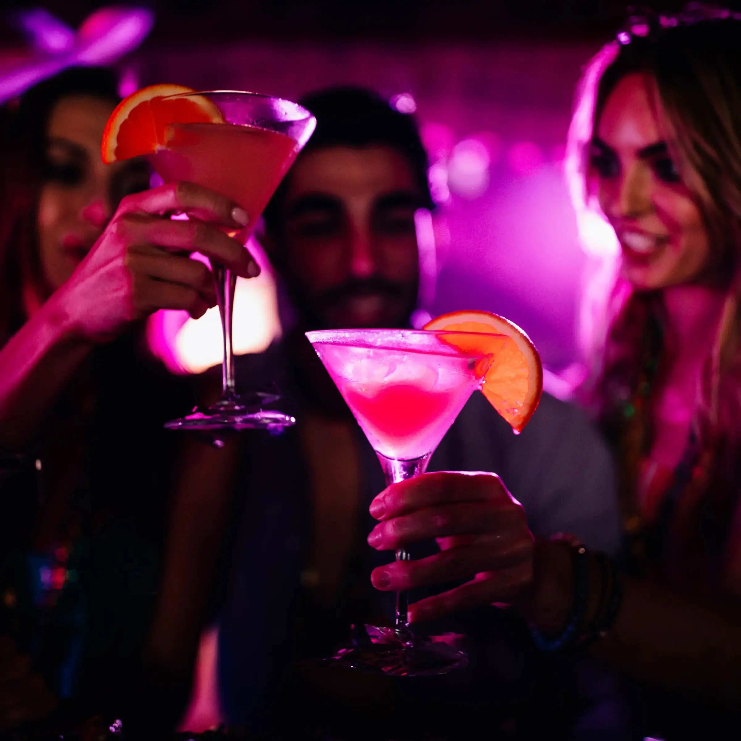 Friends toasting with pink cocktails under magenta bar lights
